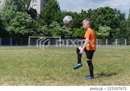 Boy juggling soccer ball on grassy field in sunlight. 125307672