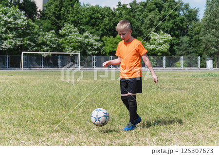 Boy kicking soccer ball on sunny grassy field. 125307673