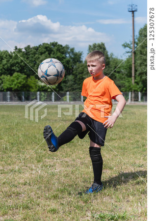 Boy juggling soccer ball on grassy field in sunlight. 125307678