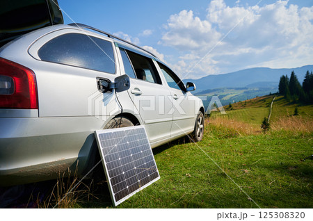 Solar panel connected via charging cable to car's charging port. Transition from internal combustion engines to electric cars, Renewable energy sources and sustainable transportation solutions. Solar panel connected via charging cable to car's charging port. Transition from internal combustion engines to electric cars, Renewable energy sources and sustainable transportation solutions. 125308320