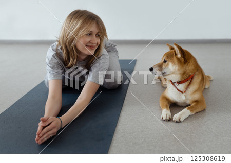 The dog practices yoga in the cobra pose in the studio. Young women meditating with pet The dog practices yoga in the cobra pose in the studio. Young women meditating with pet 125308619
