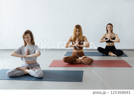 Group athletic attractive girls sit in lotus position on yoga mat indoors .Yoga, fitness and healthy lifestyle Group athletic attractive girls sit in lotus position on yoga mat indoors .Yoga, fitness and healthy lifestyle 125308691