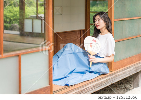 古民家の縁側に座って、団扇で扇いで涼む若い女性 古民家の縁側に座って、団扇で扇いで涼む若い女性 125312656