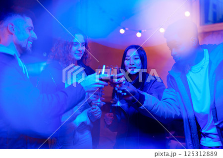 Friends celebrating with drinks at a lively gathering in a cozy location during the evening 125312889