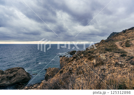 Cloudy coastal landscape with rocky shore and gentle waves under a moody sky during late afternoon Cloudy coastal landscape with rocky shore and gentle waves under a moody sky during late afternoon 125312898