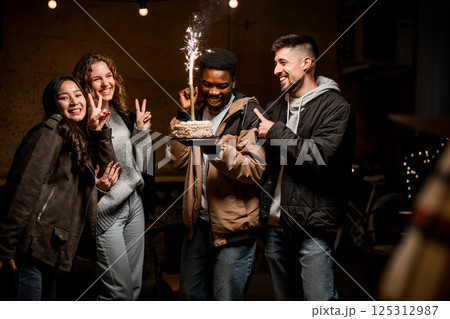 Friends celebrating with a cake and sparkler at a cozy indoor gathering during an evening event Friends celebrating with a cake and sparkler at a cozy indoor gathering during an evening event 125312987