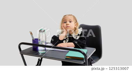Bored girl resting head on hand while sitting at school desk with pencils, books and water bottle. Concept of school fatigue 125313007