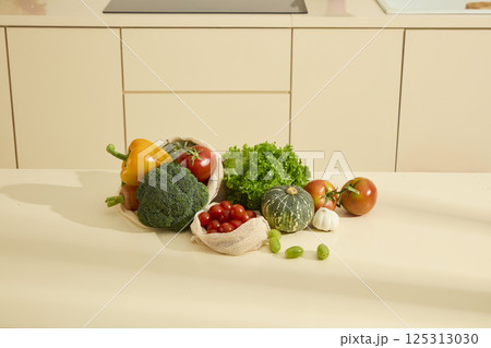 Lettuce, broccoli, bell peppers, carrots, pumpkin, tomatoes, garlic, and a mesh bag of cherry tomatoes cluster on a table. Green grapes line the other vegetables. Fresh organic food in the kitchen. 125313030