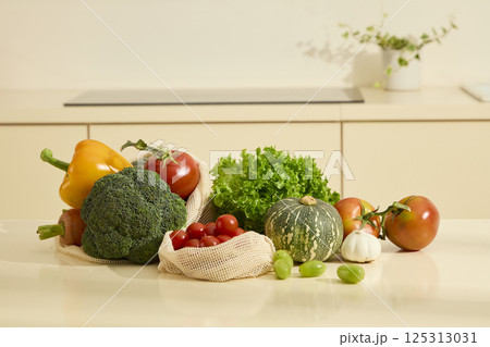 Front view of freshly harvested organic vegetables, including green plants, cauliflower, squash, tomatoes and bell peppers. Presenting on white kitchen countertop, daylight shining on objects. 125313031