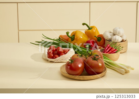 Vegetables are placed in wooden bowls, shown on the kitchen counter. Bell peppers, garlic, chili peppers and tomatoes are all fresh and colorful. A bunch of green onions is placed in the middle. 125313033