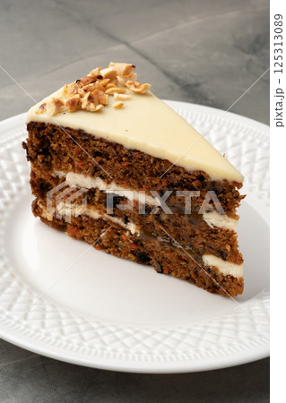 Delicious slice of layered carrot cake with cream cheese frosting served on a decorative plate 125313089