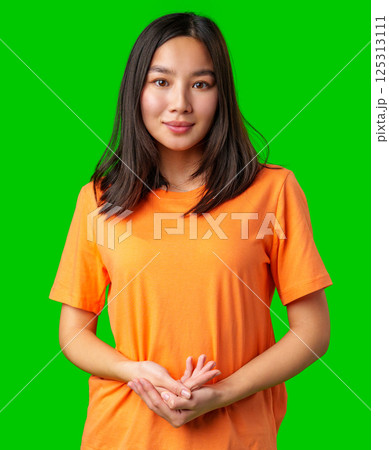 Young woman in an orange t-shirt poses confidently against a bright green backdrop indoors 125313111