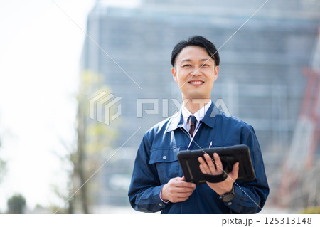 タブレット端末を持って大規模な工事現場の前に立つ業者 125313148