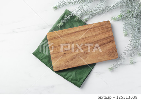 Wooden plate board on linen napkin with green leaves on marble table, top view 125313639