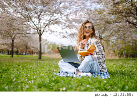 Beautiful female student is using laptop, notepad to prepare for outdoor classes. Education concept. 125313685