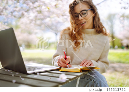 Happy woman relaxing in park, writing in notebook, sitting with laptop. Weekend, spring concept. 125313722