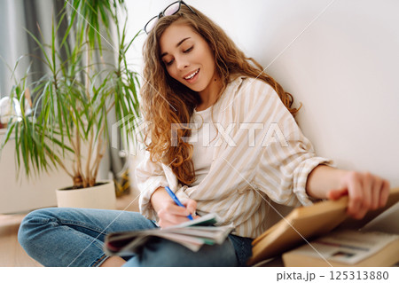 Happy woman sitting on floor in living room, enjoying reading book. Concept of relaxation, comfort. 125313880