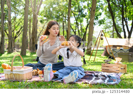 Mother and child having a delicious meal together while camping in a sunny wooded area 125314480