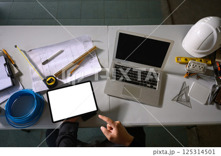 Top view of engineer using digital tablet at desk surrounded by measuring tools and blueprints Top view of engineer using digital tablet at desk surrounded by measuring tools and blueprints 125314501