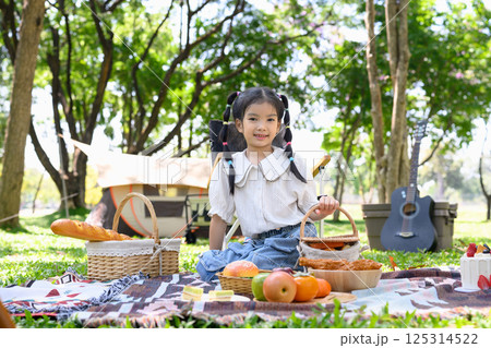 Cute little girl at a family camping picnic with picnic baskets and fresh food Cute little girl at a family camping picnic with picnic baskets and fresh food 125314522