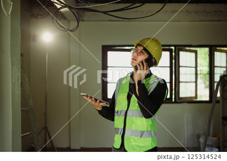 Construction manager on phone call while inspecting ceiling wiring during renovation project Construction manager on phone call while inspecting ceiling wiring during renovation project 125314524