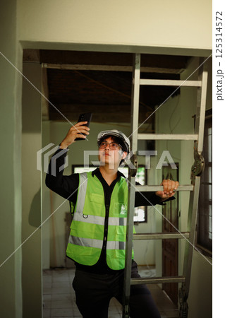 Construction worker standing by ladder, capturing photos of renovation site 125314572