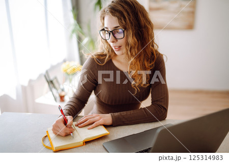Young woman uses laptop at home, looks at screen, reads or writes at table. The concept of education 125314983
