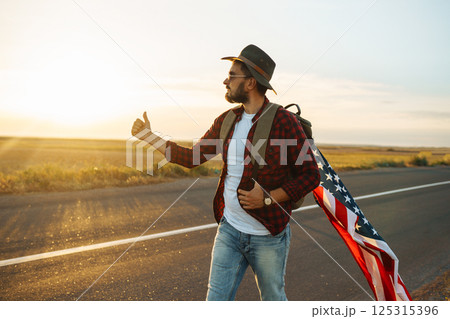 4th of July. American Flag. Traveler with the flag of America. The man in a hat, a backpack, a shirt and jeans. 4th of July. American Flag. Traveler with the flag of America. The man in a hat, a backpack, a shirt and jeans. 125315396