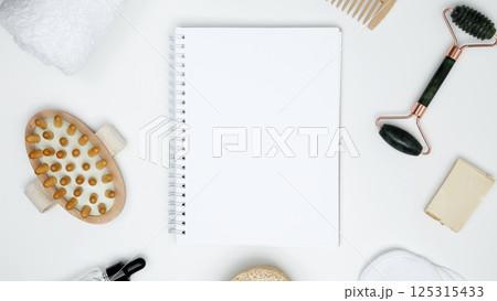 Mock up white notebook, sustainable self-care concept. Eco-friendly beauty products: massage brush, loofah, marble roller, towel, reusable cotton pads 125315433