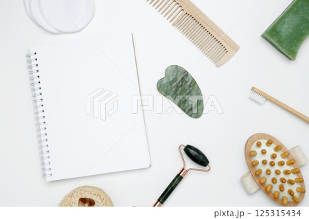 Eco-friendly beauty products: massage brush, loofah, marble roller, towel, reusable cotton pads, mock up white notebook, sustainable self-care concept 125315434