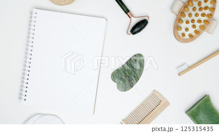 Mock up white notebook, sustainable self-care concept. Eco-friendly beauty products: massage brush, loofah, marble roller, towel, reusable cotton pads 125315435