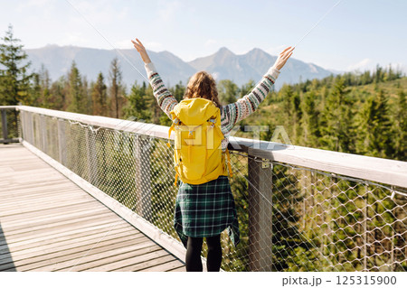 Happy woman with yellow backpack on wooden pedestrian bridge enjoying mountain scenery. Happy woman with yellow backpack on wooden pedestrian bridge enjoying mountain scenery. 125315900