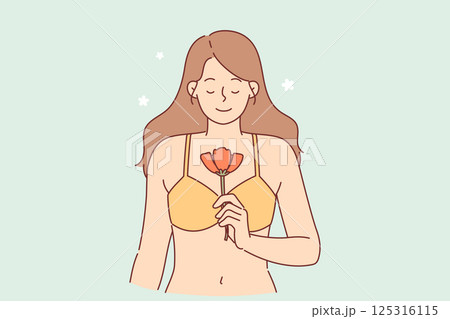 Serene woman holds spring flower and smiles, standing in bra, for metaphor of purity and innocence Serene woman holds spring flower and smiles, standing in bra, for metaphor of purity and innocence 125316115