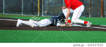 First baseman trying to tag the runner who is diving back to the bag during a pick off play 125317232