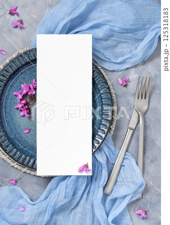 Wedding table place with a card near fabric and wild purple flowers top view on gray, spring mockup 125318183
