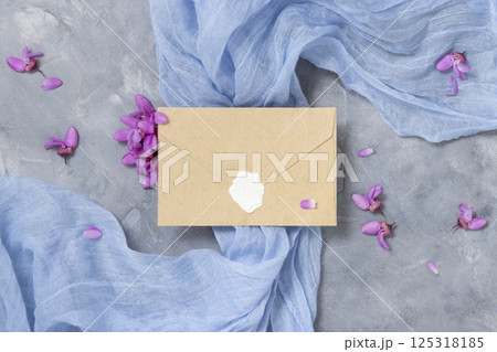 Sealed envelope on fabric near wild purple flowers top view on gray, spring wedding mockup 125318185