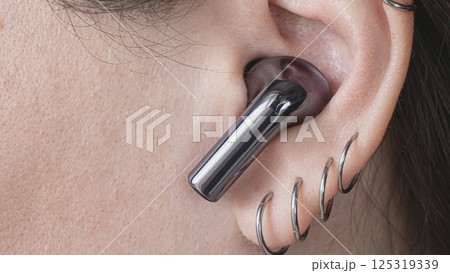 Close-up view of wireless ear buds paired with jewelry on the ear. High quality photo 125319339