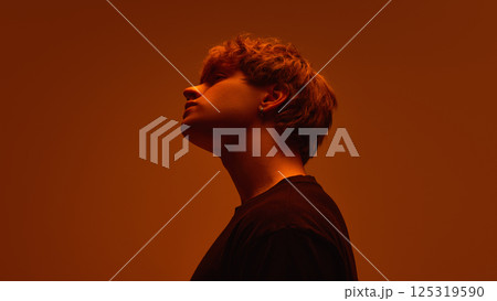 Side view of young man with tilted head with expression unreadable in soft orange haze against bright gradient background. Concept of beauty 125319590