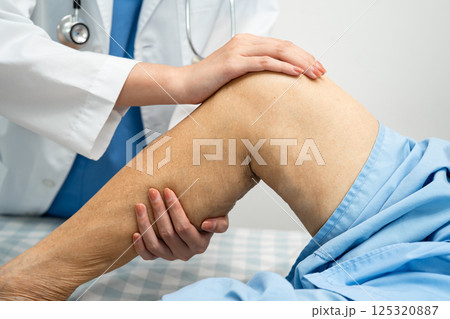 Doctor checking Asian elderly woman patient with scar knee replacement surgery in hospital. 125320887