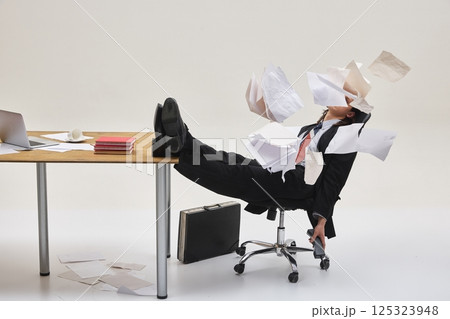 Man sitting in chair with legs on desk, surrounded by flying papers in chaotic office mess, overwhelmed by work. Dynamic photo. Man sitting in chair with legs on desk, surrounded by flying papers in chaotic office mess, overwhelmed by work. Dynamic photo. 125323948