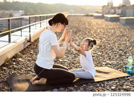 Mother and young daughter participating in outdoor exercise. Shows a bonding activity enhancing fitness, coordination, and emotional connection. Illustrates warmth, unity and healthy family lifestyle. 125324996