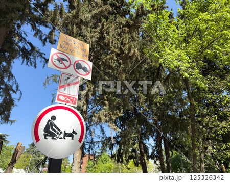 Humorous and prohibitive park signs among green trees and blue sky. Instructions include no urinating, no dogs off leash, and a pun sign, creating a quirky yet informative visual message 125326342