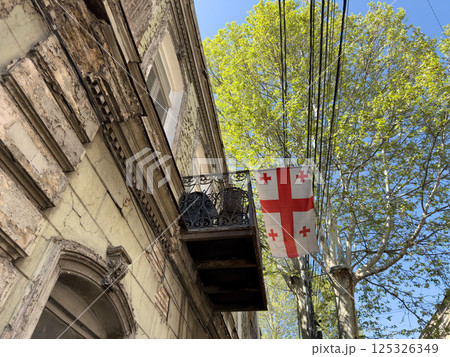 Aged building with cracked walls, cast iron balcony, and symbolic flag of Georgia evoke nostalgic mood. Warm textures and historic character highlight authentic city life under soft natural light Aged building with cracked walls, cast iron balcony, and symbolic flag of Georgia evoke nostalgic mood. Warm textures and historic character highlight authentic city life under soft natural light 125326349