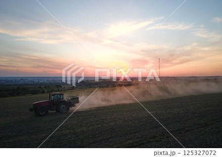 Tractor spraying fertilizers with insecticide herbicide chemicals on agricultural field at sunset Tractor spraying fertilizers with insecticide herbicide chemicals on agricultural field at sunset 125327072