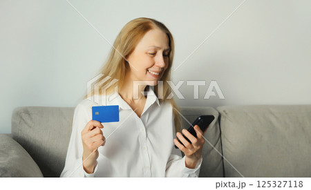 Woman holding plastic credit bank card, looking at phone, shopping online or ordering goods at home Woman holding plastic credit bank card, looking at phone, shopping online or ordering goods at home 125327118