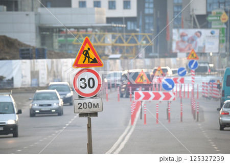 Roadworks warning traffic signs of construction work on city street and slowly moving cars Roadworks warning traffic signs of construction work on city street and slowly moving cars 125327239