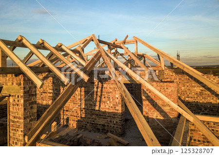 Private residential house with wooden roof frame structure under construction. Unfinished brick building under development. 125328707