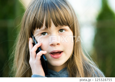 Portrait of pretty child girl with long hair talking on cell phone. Little female kid communicating using smartphone. Children communication concept. Portrait of pretty child girl with long hair talking on cell phone. Little female kid communicating using smartphone. Children communication concept. 125328755