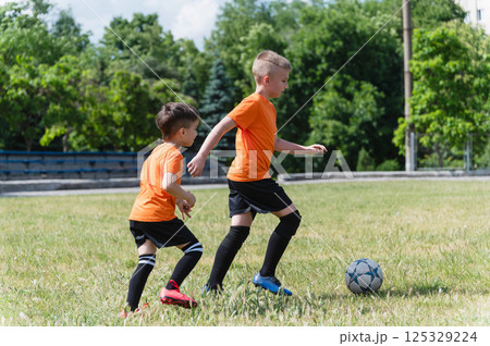Two boys running after soccer ball on green field. 125329224