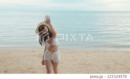 Beautiful Asian woman wear sungrass and hat turning back running to tropical paradise beach, Happy female in bikini having fun with hand to camera inviting you come with me 125329570